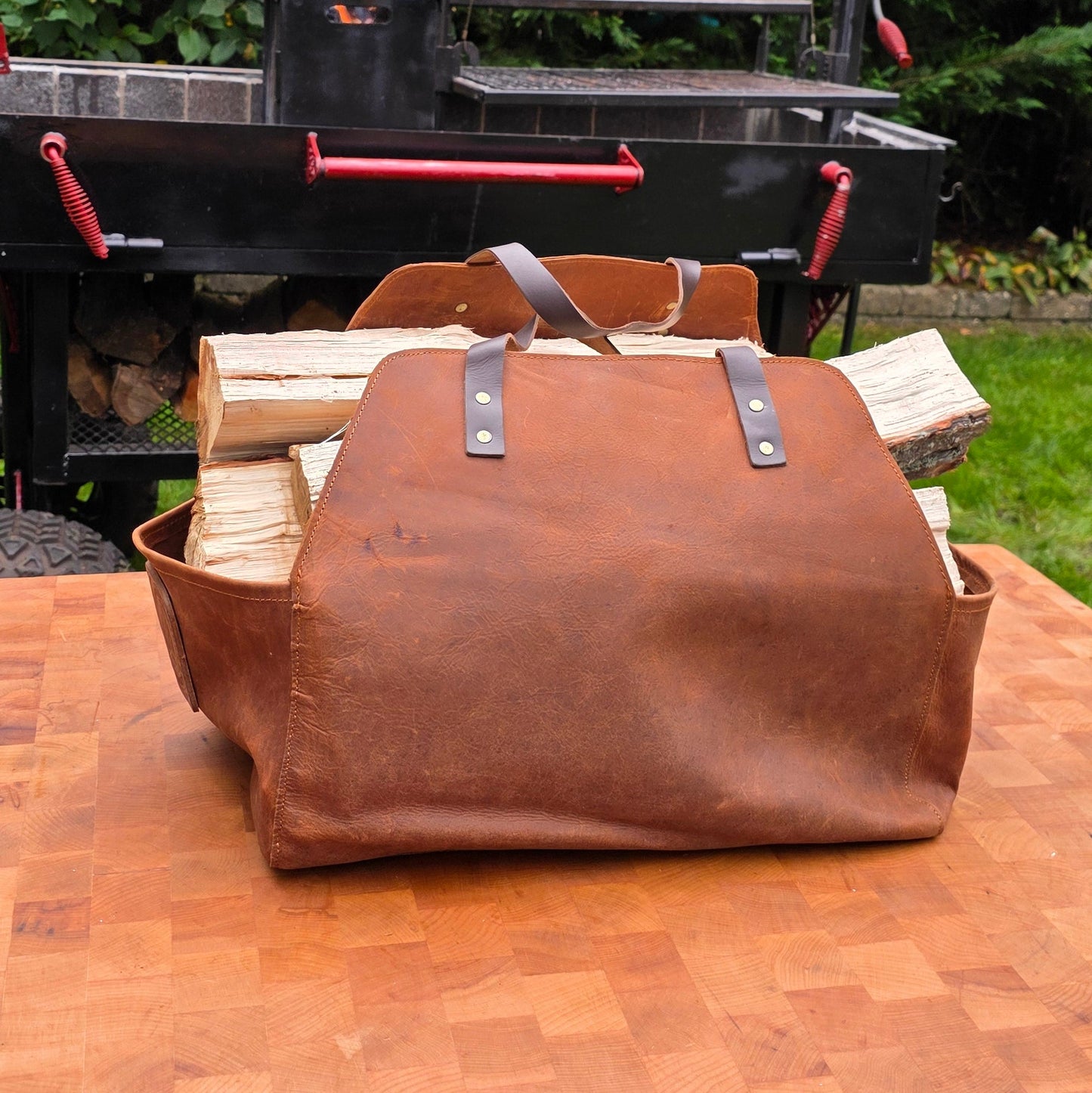 Gotham City Leather split carrier in burgundy full-grain leather displayed with custom Santa Maria grill and fire pit in professional backyard BBQ setup