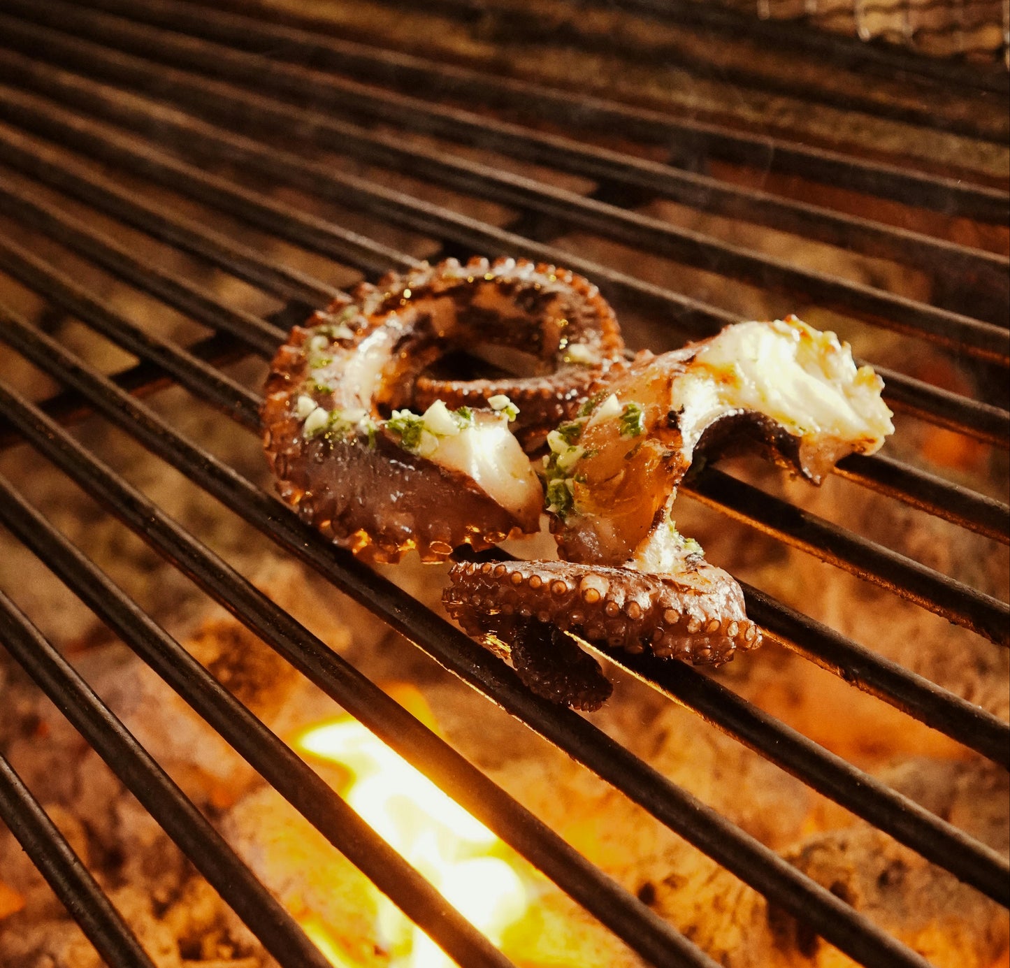 Grilled octopus on a barbecue grill with flames below Mike Riddle Chef
