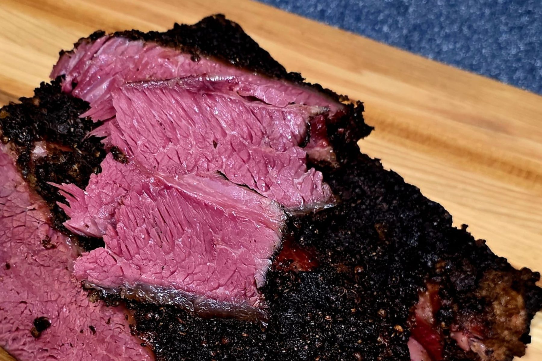 Beef rib pastrami with black pepper coriander crust and pink smoke ring on wooden cutting board - NY BBQ Guys signature recipe