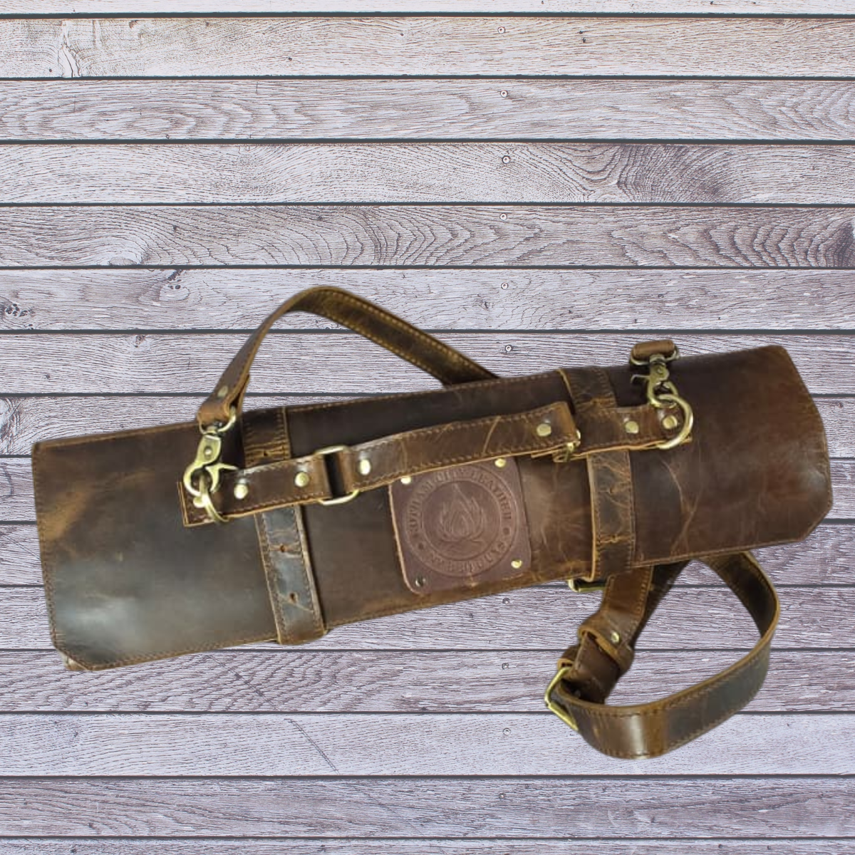 Brown leather tool roll with Brass accents on a wooden surface