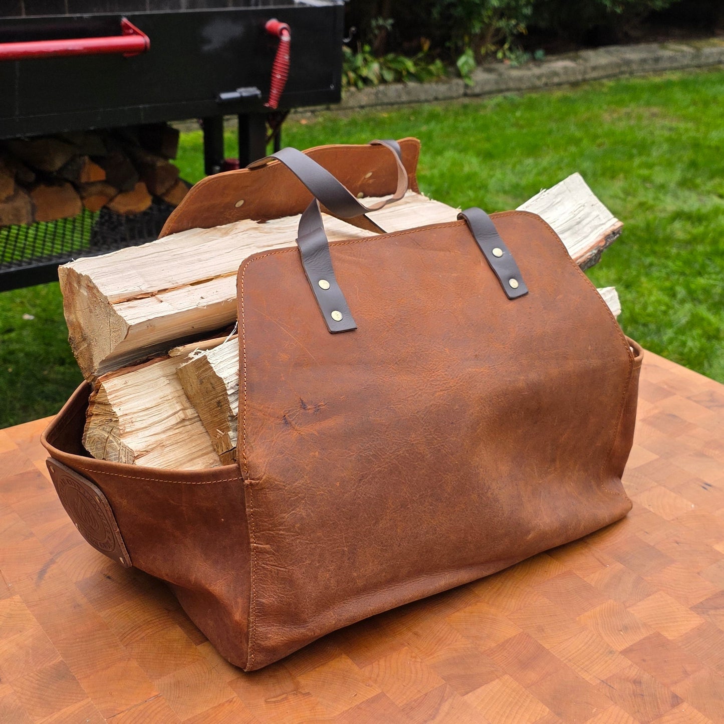 Gotham City Leather full-grain leather firewood carrier filled with split wood showing utility and craftsmanship in outdoor backyard BBQ setting