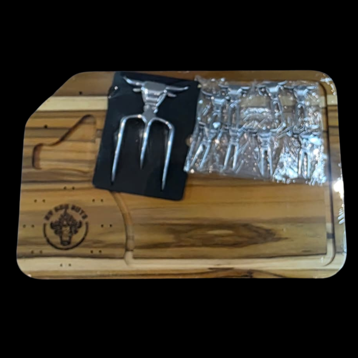 Wooden cutting board with a meat fork, black card, and glass on a dark background